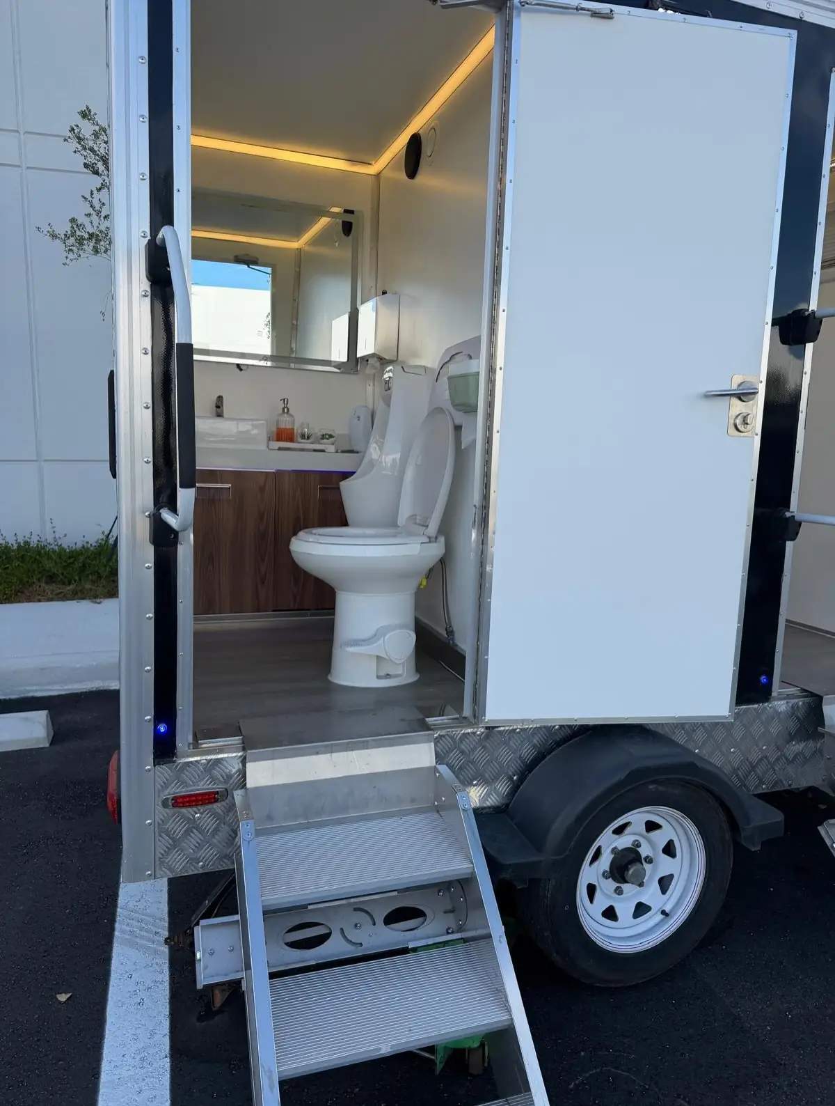 Open door of a luxury restroom trailer showing the toilet and lit vanity