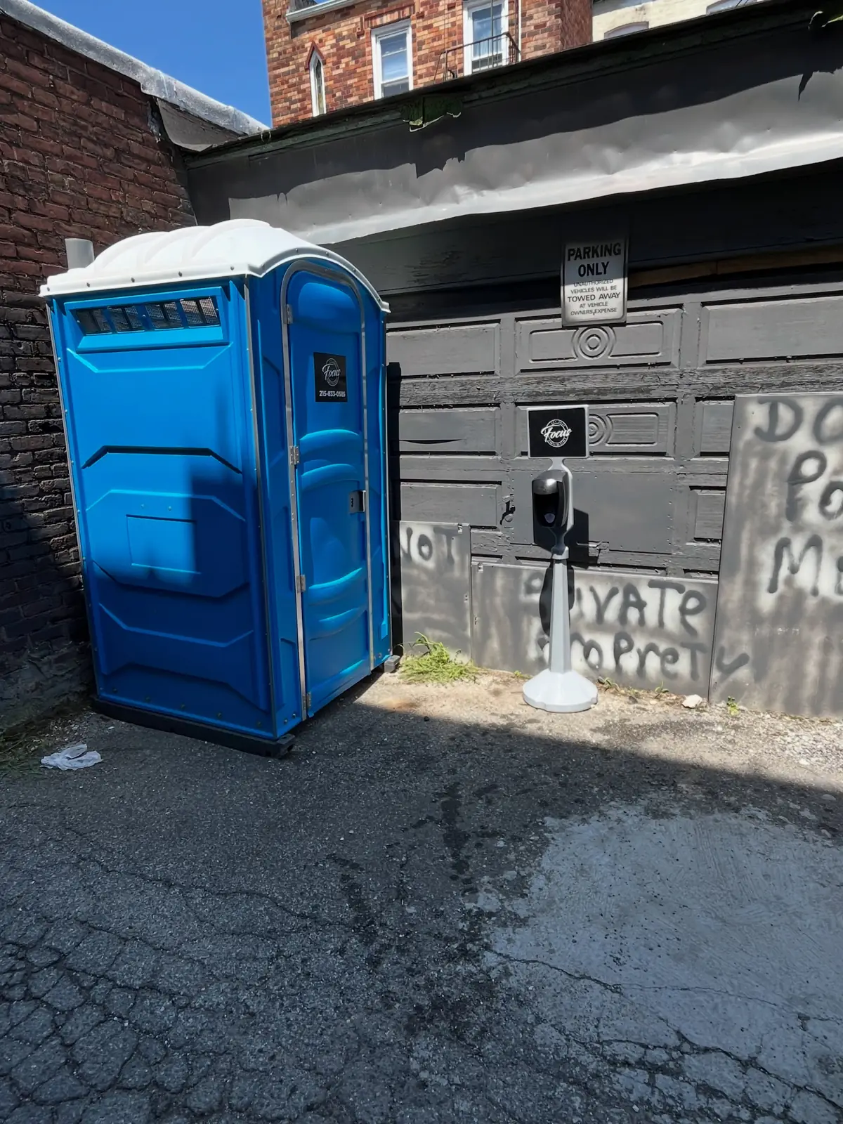 Standard porta potty in a paved alley beside a building