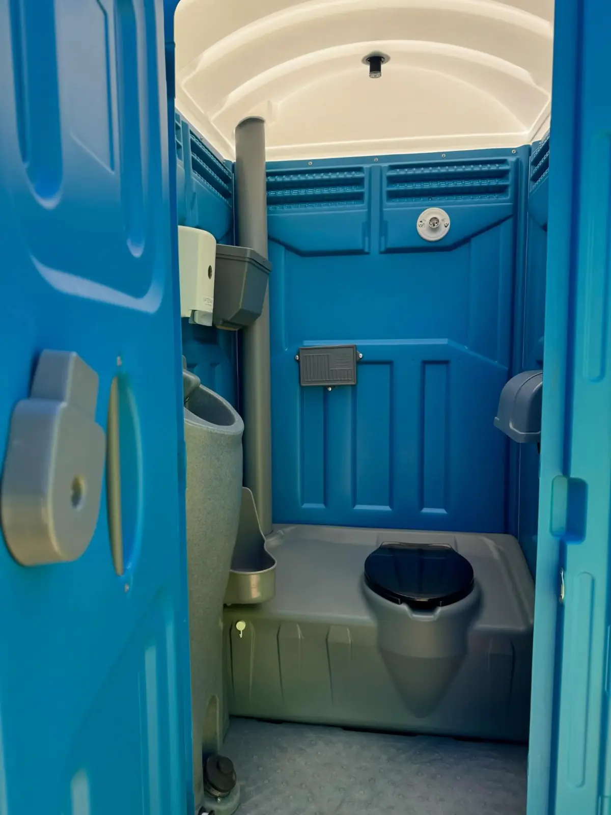 Inside a blue standard porta potty showing the urinal and toilet paper holder